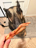 Load image into Gallery viewer, Duck Feet ABF dog treat by Naked Beasts; dark-coated dog taking a duck foot from a hand