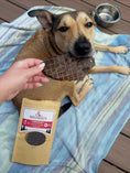Load image into Gallery viewer, Lamb Liver Thin Cut dog treat by Naked Beasts; dark rectangular piece held near a dog with Naked Beasts packaging