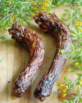 Load image into Gallery viewer, Turkey Neck by Naked Beasts, two dried necks on a wooden cutting board, surrounded by green herbs.