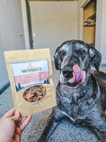 Load image into Gallery viewer, Green Lipped Mussels dog treats by Naked Beasts in a beige pouch with a window, beside a brindle dog licking its lips.