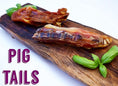 Load image into Gallery viewer, Two pork tails from Naked Beasts on a wooden board with fresh basil.