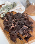 Load image into Gallery viewer, Pork heart thin-cut slices with fat trimmed, dark cured meat on a wooden board with eucalyptus leaves