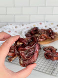Load image into Gallery viewer, Beef Pizzle loops, dried dark red chews; twisted coils on rack