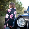 Load image into Gallery viewer, Jeffers Expression oversized fleece throw blanket with pink rose print on black, draped over shoulders beside a car.