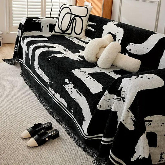 Boho couch cover in black and white chenille on sofa; fringe edges; pair of black mules nearby.