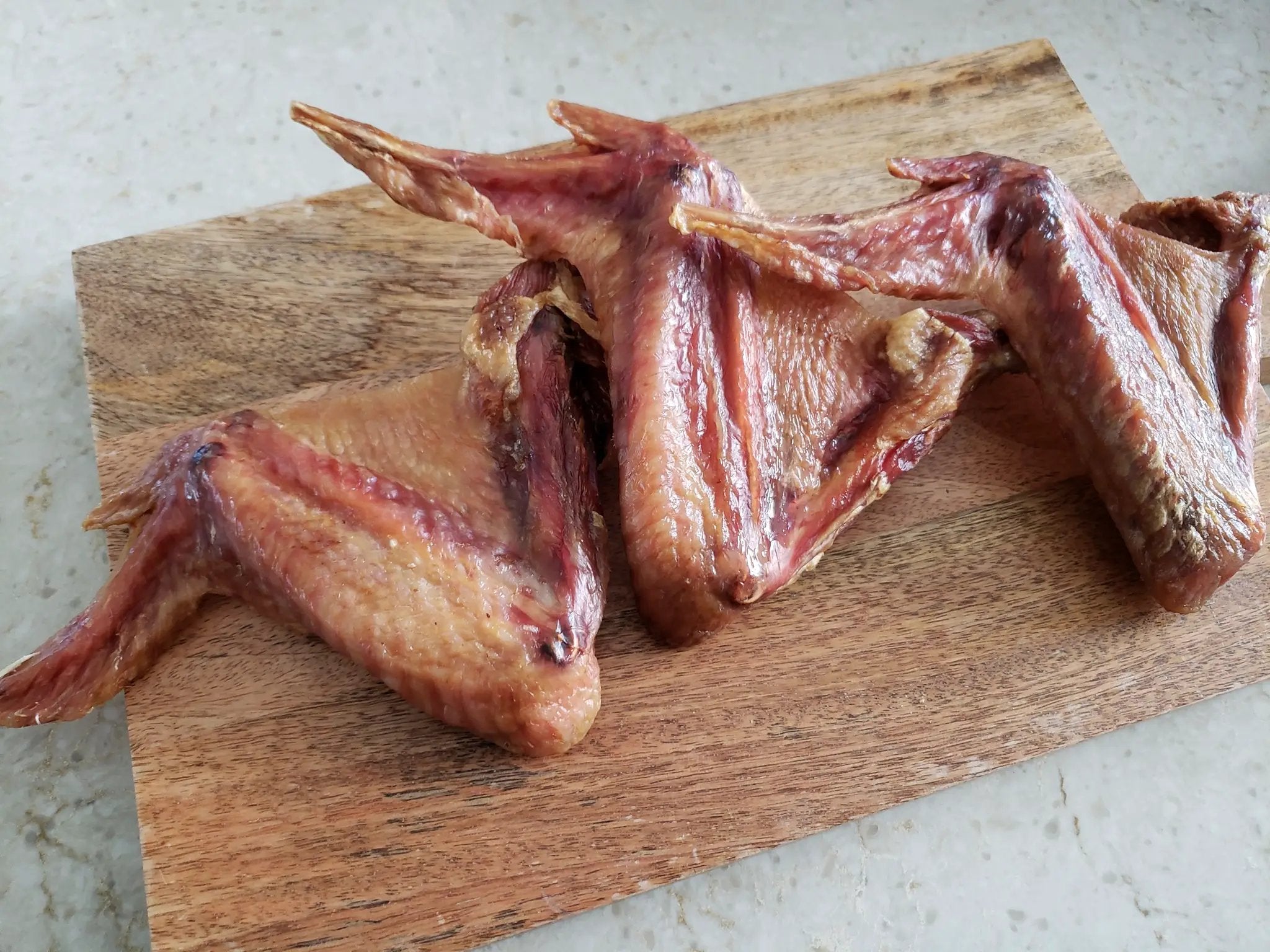 Turkey wings from Naked Beasts on a wooden cutting board, raw, skin-on, reddish-pink.
