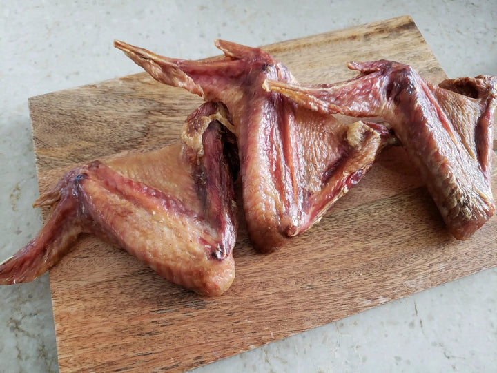 Turkey wings from Naked Beasts on a wooden cutting board, raw, skin-on, reddish-pink.