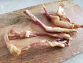Load image into Gallery viewer, Beef tendon pieces (whole and halved) on a wooden cutting board; pale pink, raw
