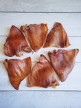 Carica l'immagine nel visualizzatore della galleria, Pig Ears by Naked Beasts, brown dried pork ears on white wooden surface
