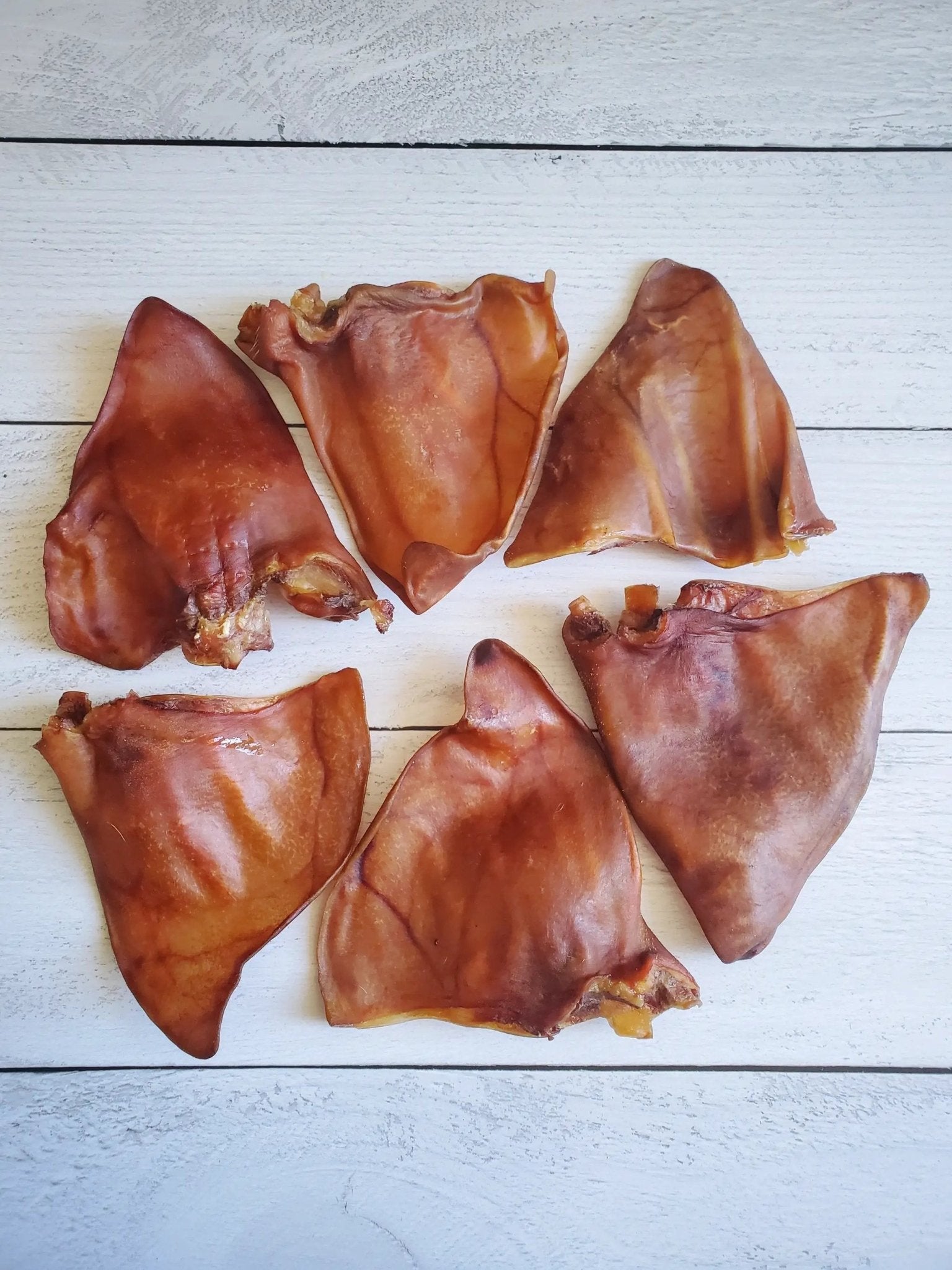 Pig Ears by Naked Beasts, brown dried pork ears on white wooden surface