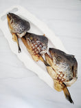 Carica l'immagine nel visualizzatore della galleria, Salmon head halves on a white platter, dark gray skin with patterned scales
