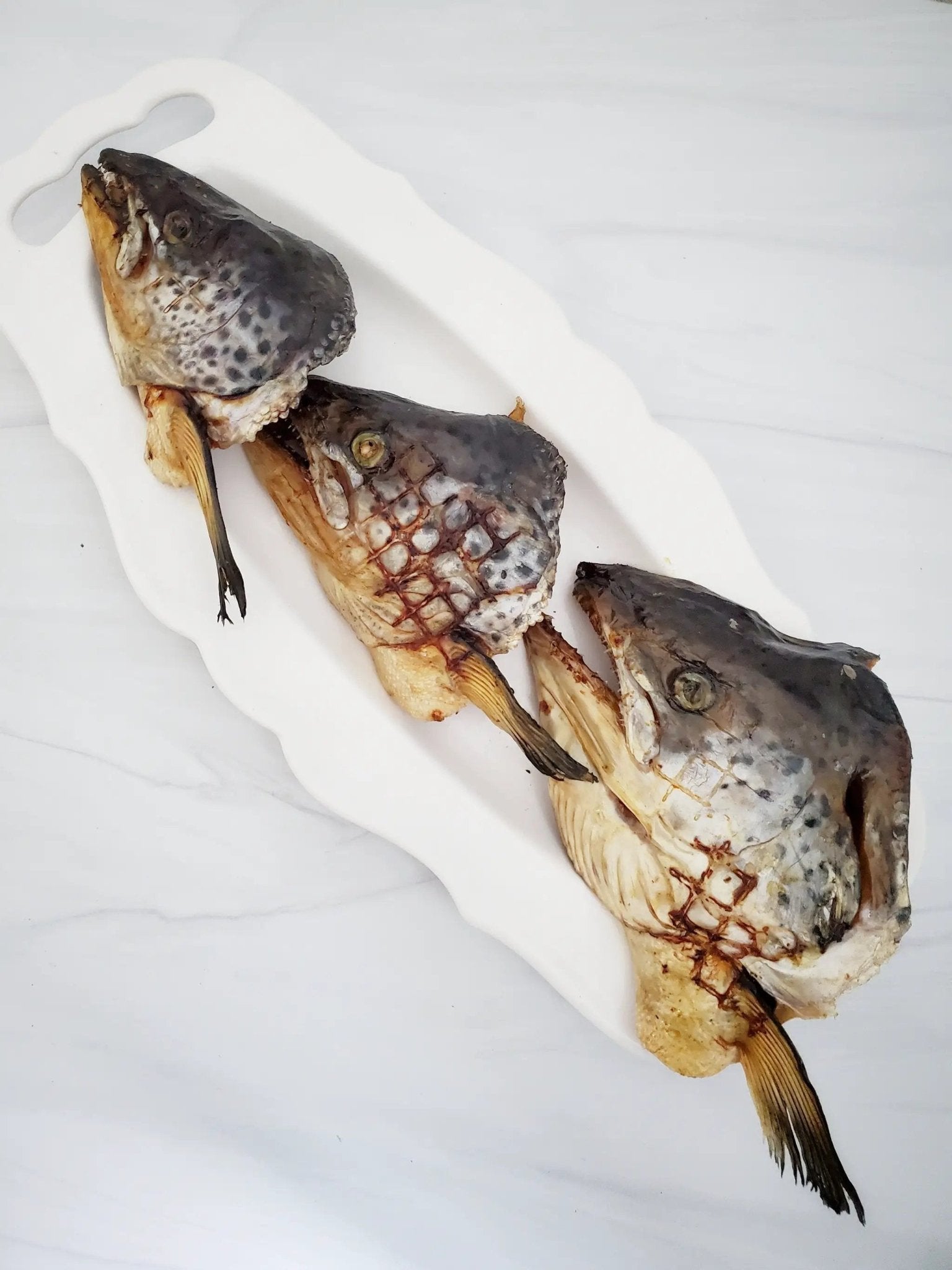Salmon head halves on a white platter, dark gray skin with patterned scales