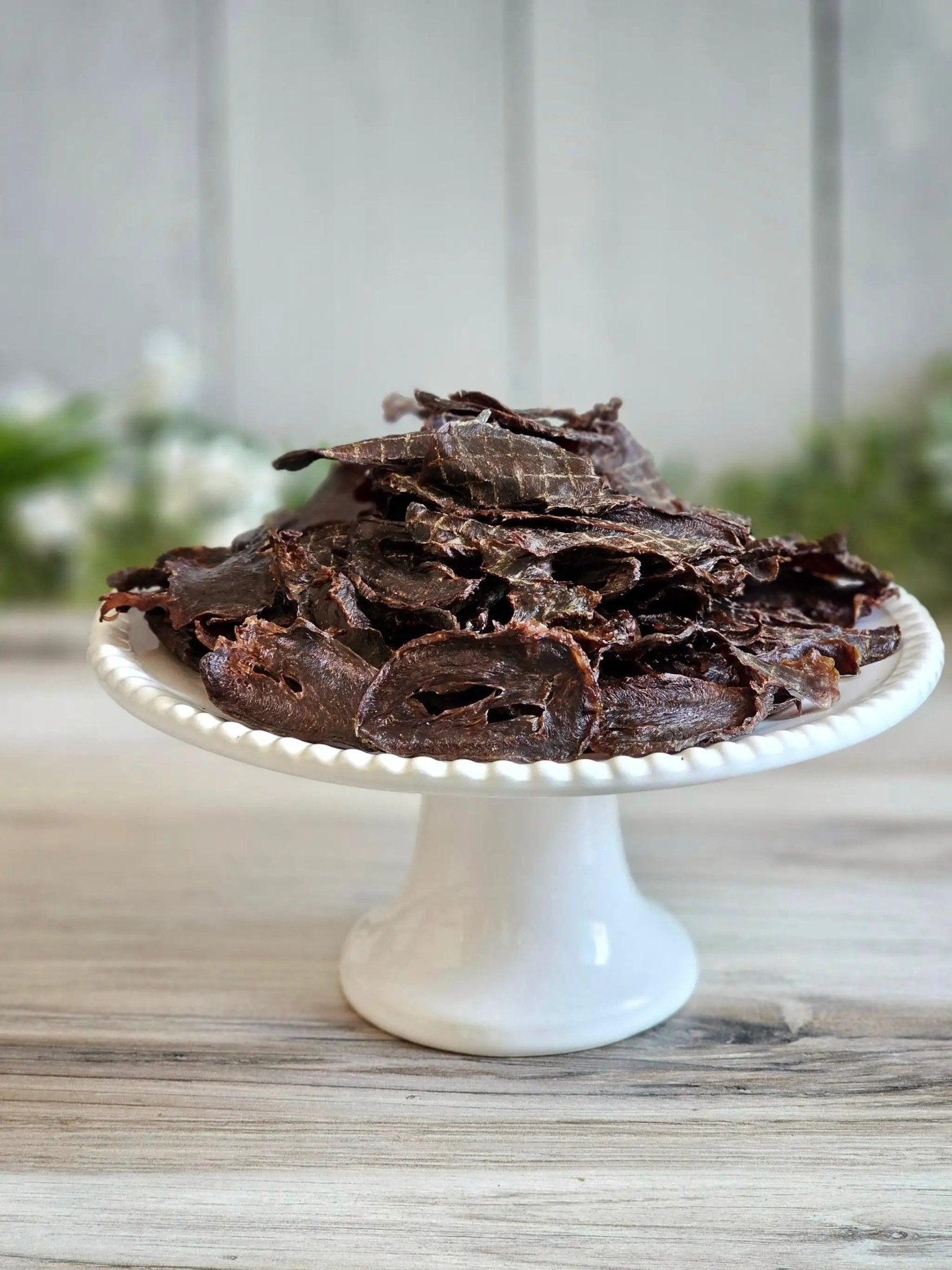Turkey Heart sliced jerky for small animals; dark brown dried treats on a white cake stand.