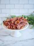 Carica l'immagine nel visualizzatore della galleria, Pig ears by Naked Beasts, piled on a white cake stand with brown dried slices.
