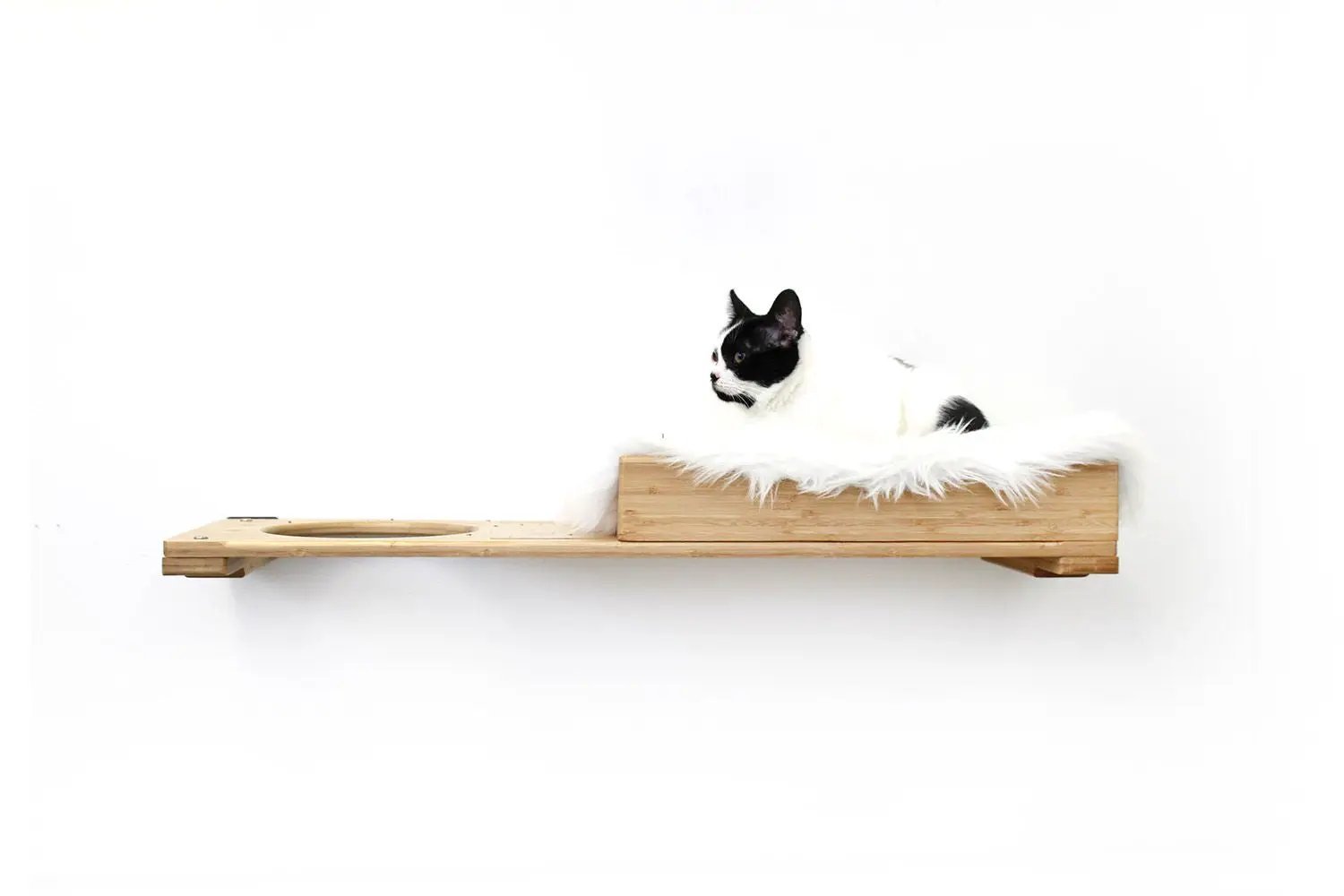 The Cat Nest Bed on a natural wood cat shelf with white faux fur lining and a black-and-white cat.