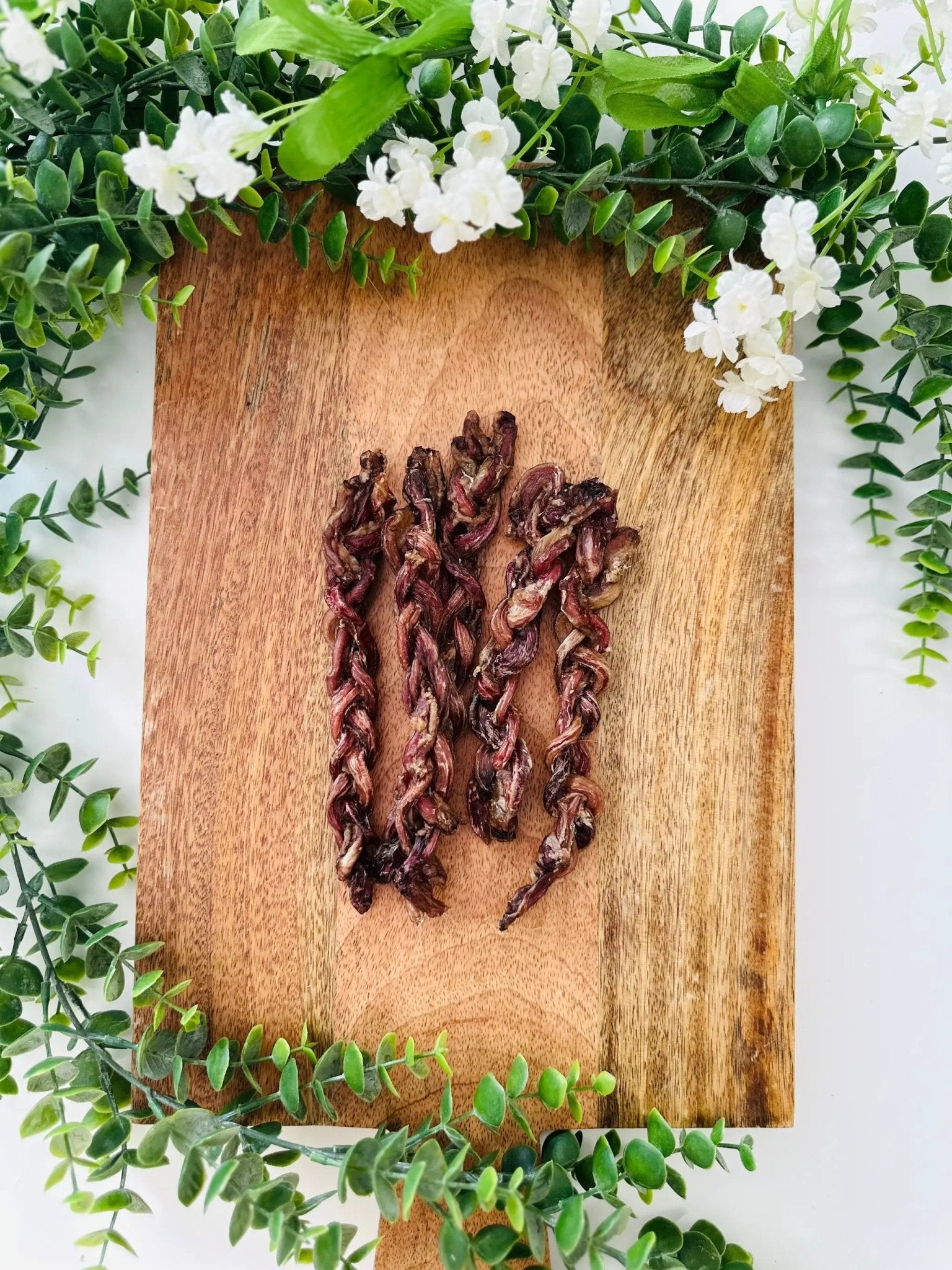 Lamb Pizzle by Naked Beasts, Limited Edition, reddish-brown dried twists on a wooden board with green foliage.
