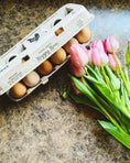 Load image into Gallery viewer, Henlay Laid Local egg carton with 12 brown eggs beside pink tulips on a marbled countertop
