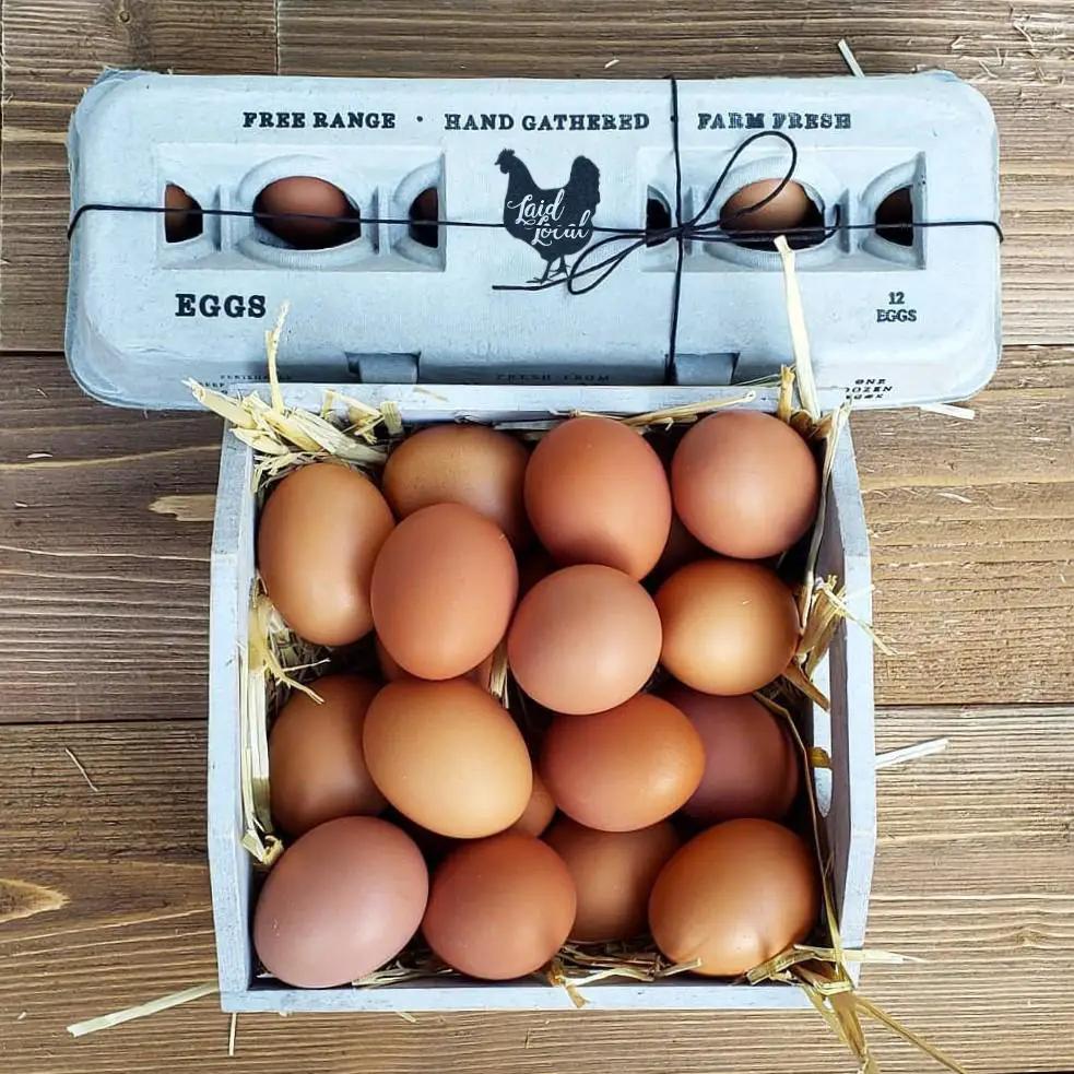 Henlay Laid Local egg cartons with vintage printed design; brown eggs in a straw-filled wooden crate