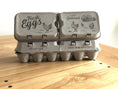 Load image into Gallery viewer, Pair of split-apart egg cartons holding 6 or 12 extra-large eggs; kraft packaging with farm illustrations
