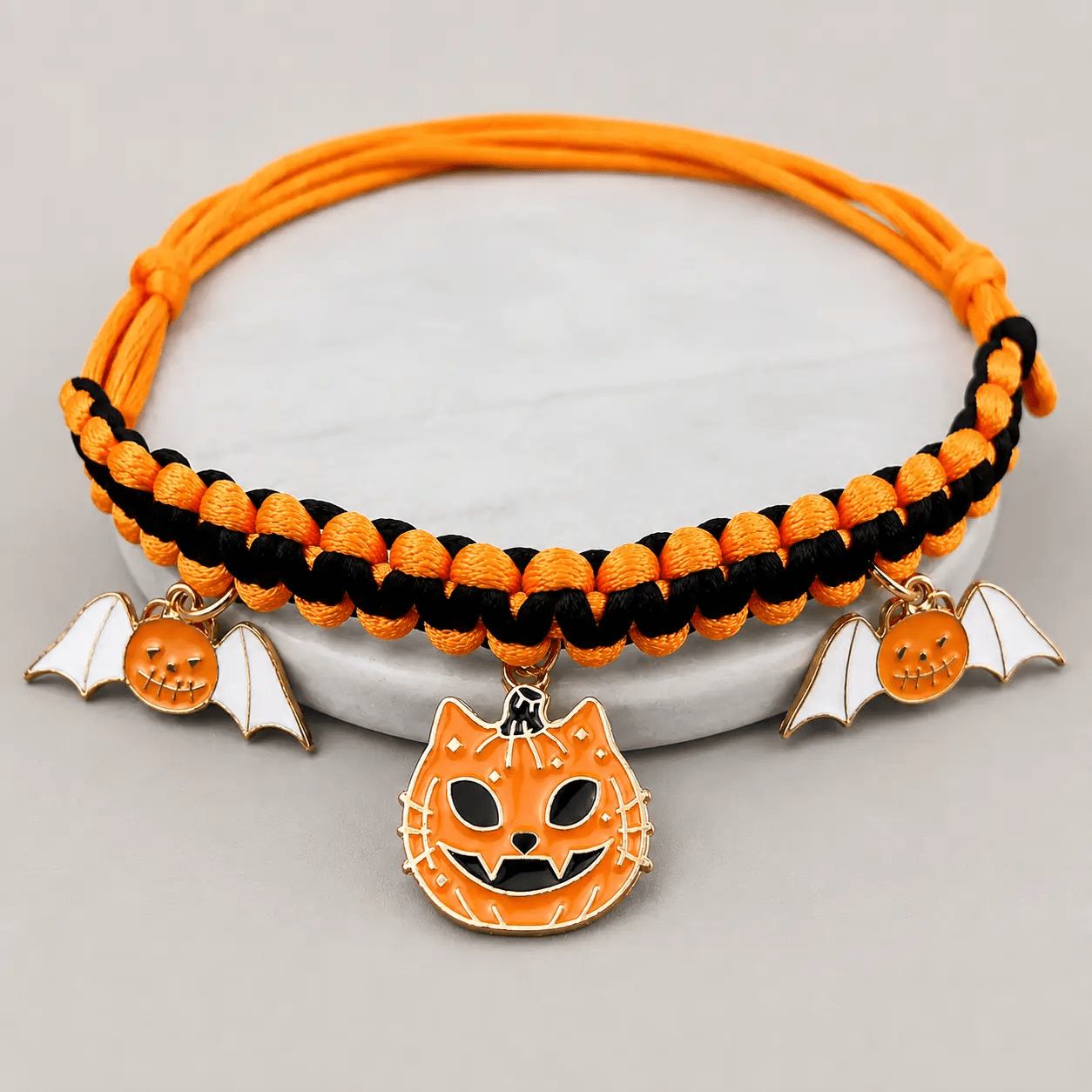 Halloween hand-woven pet collar decoration in orange and black with three charms: pumpkin and two bats.