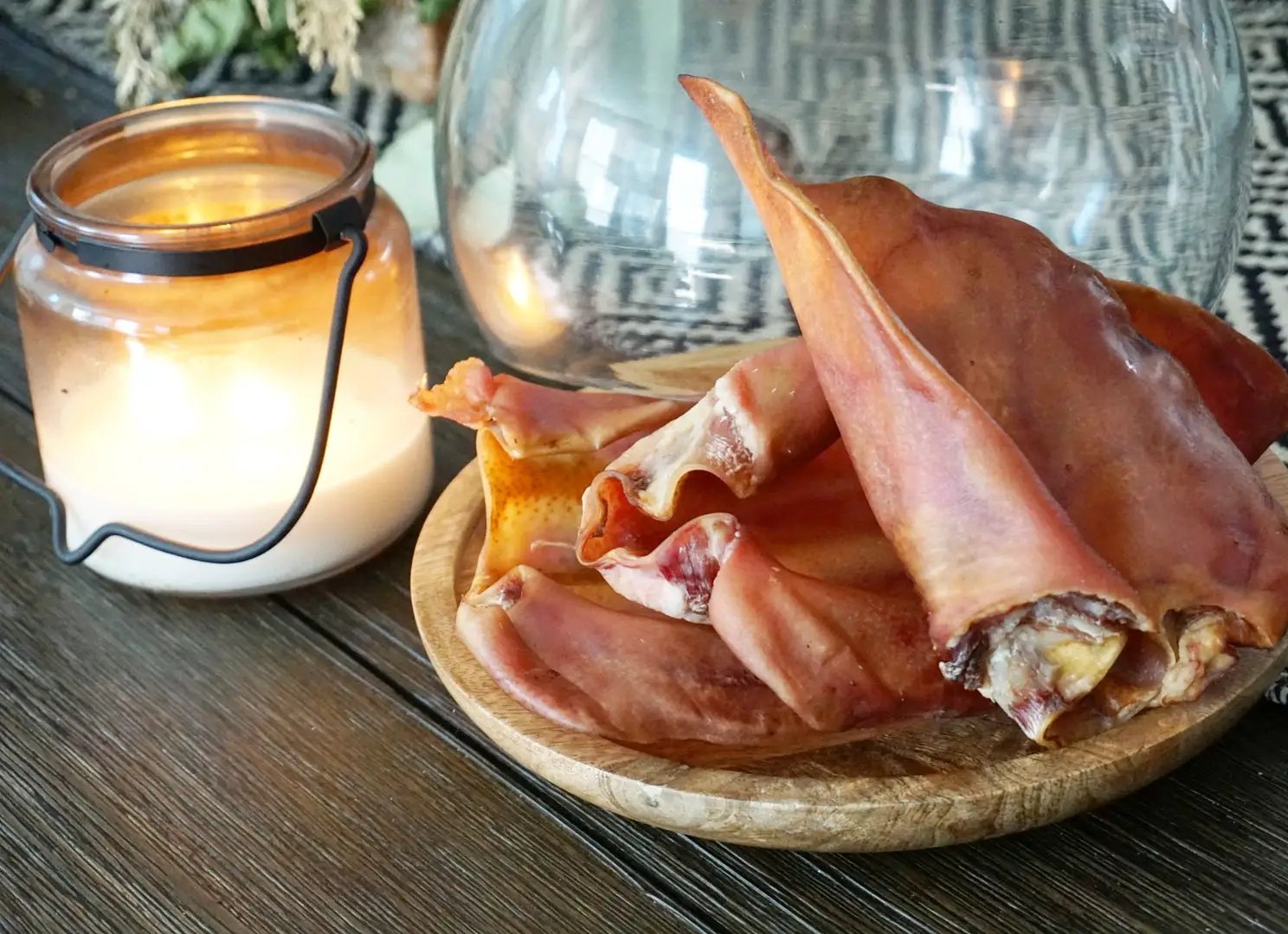 Pig Ears by Naked Beasts; several pink pig ears on a wooden board beside a lit candle