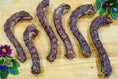 Load image into Gallery viewer, Duck necks; six dark dried jerky sticks on a wooden board with floral accents.

