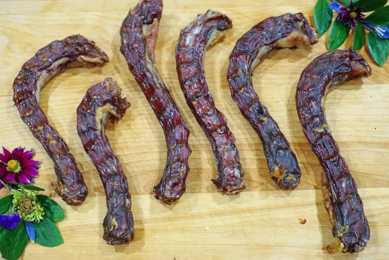Duck necks; six dark dried jerky sticks on a wooden board with floral accents.