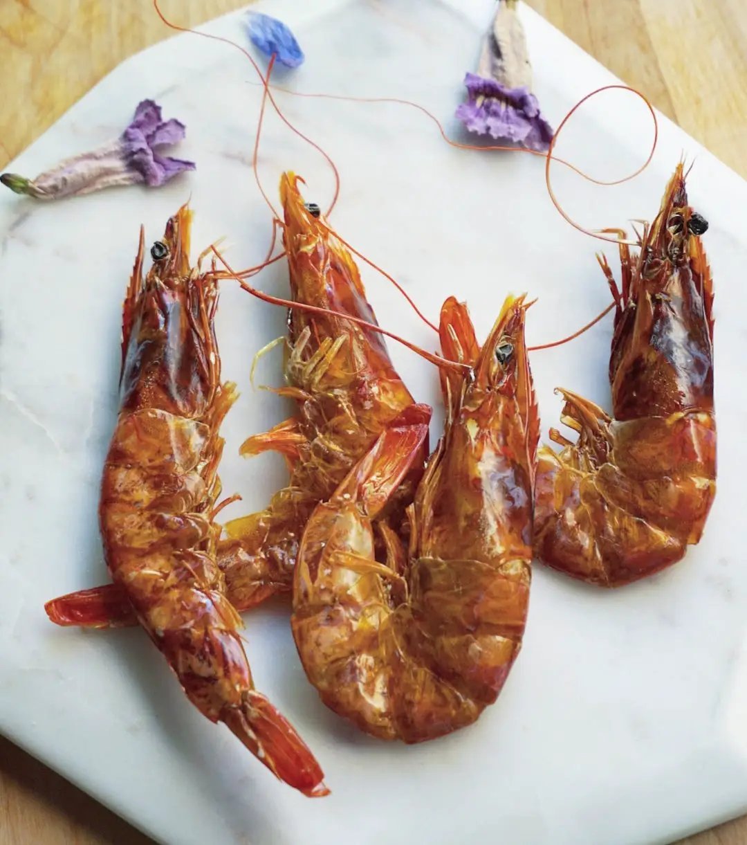 Shrimp by Naked Beasts; four orange-red cooked prawns on a marble board