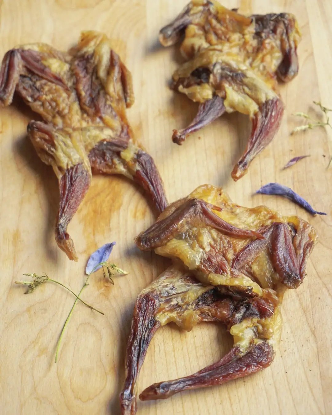 Naked Beasts Whole Quails (Bone-In), 4 roasted brown poultry pieces on a wooden board
