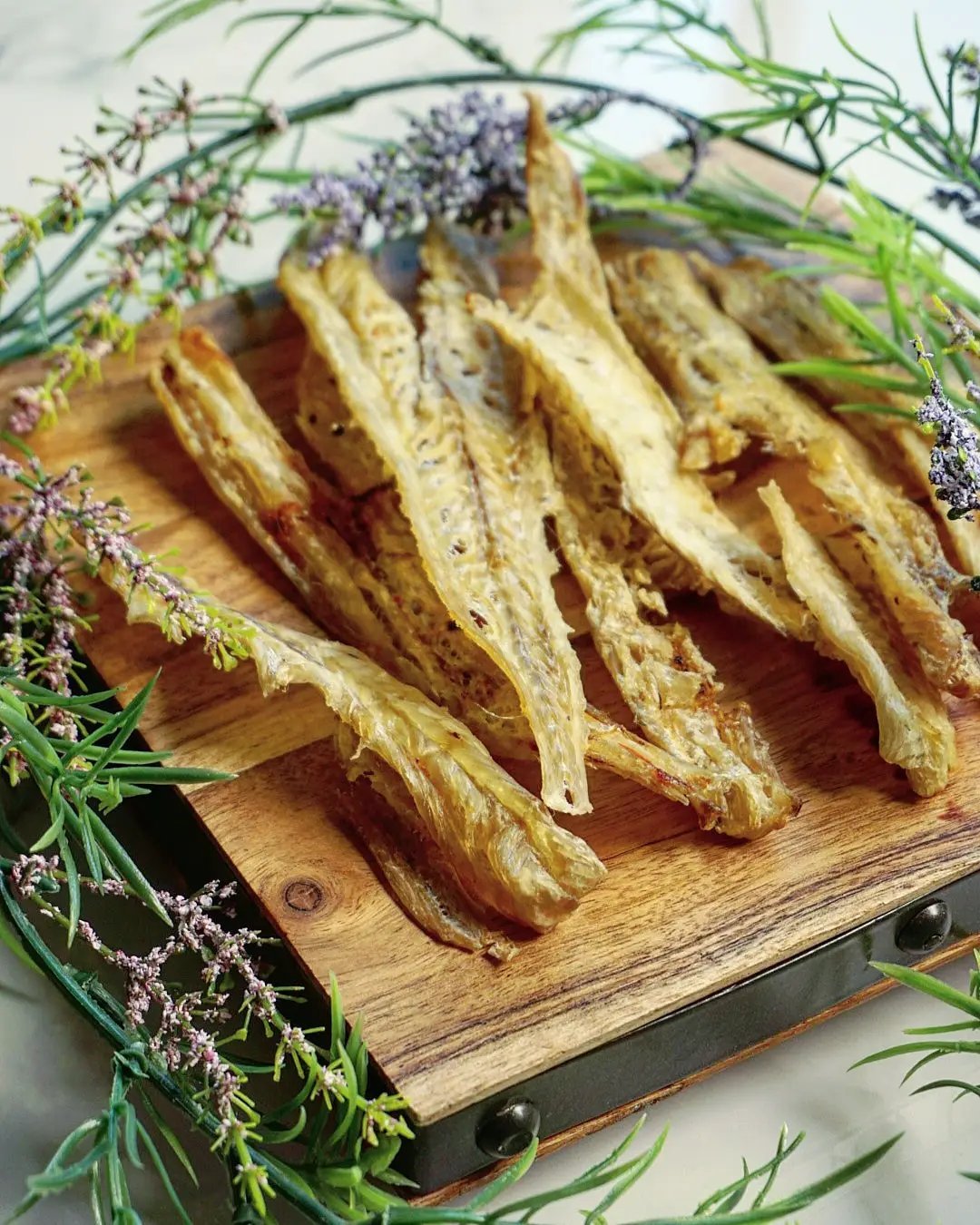 Pollock dried fish jerky, wild-caught, Naked Beasts, arranged on a wooden board with fresh herbs.
