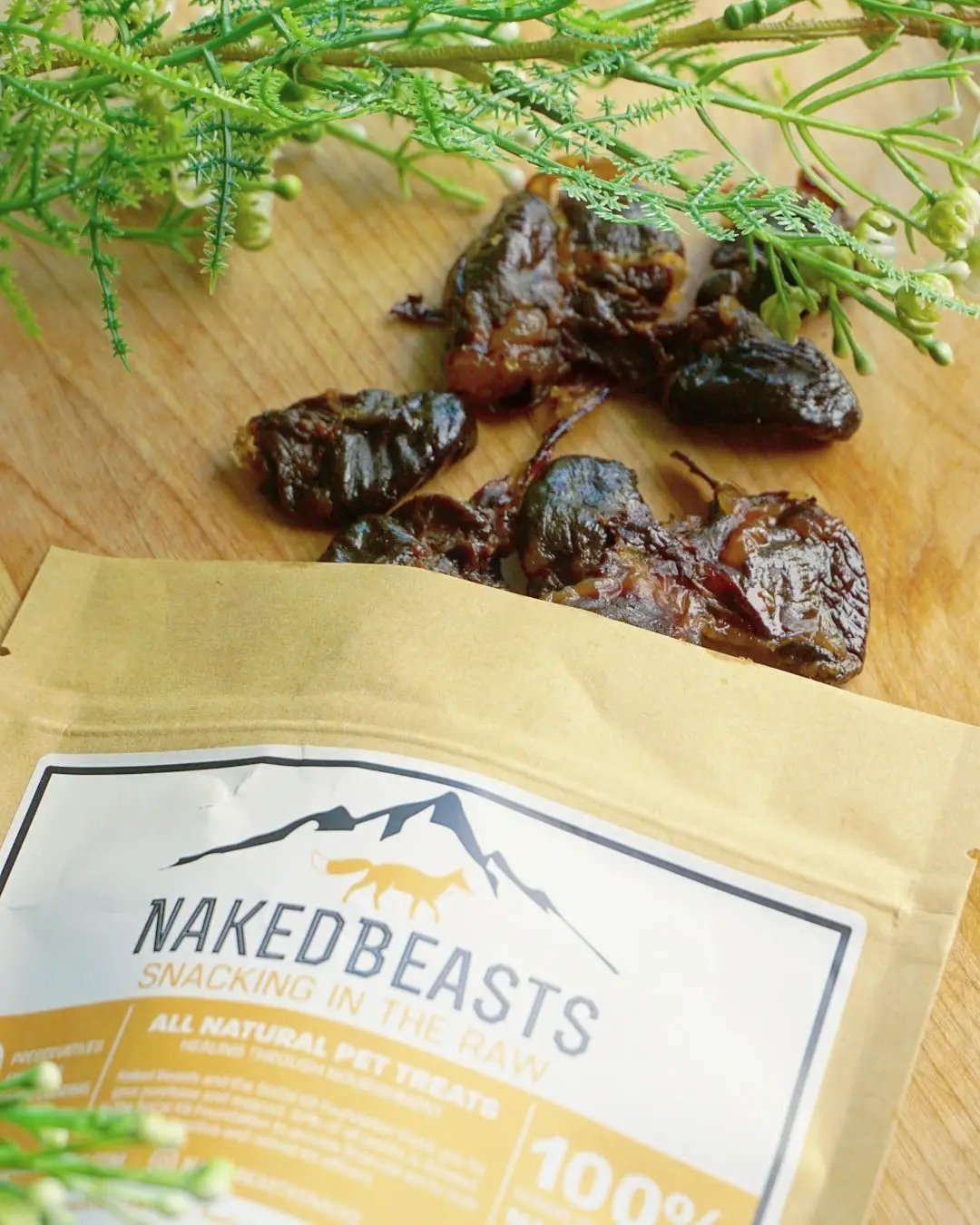 Naked Beasts Duck Hearts ABF dried pet treats on a wooden board beside the brand label packaging