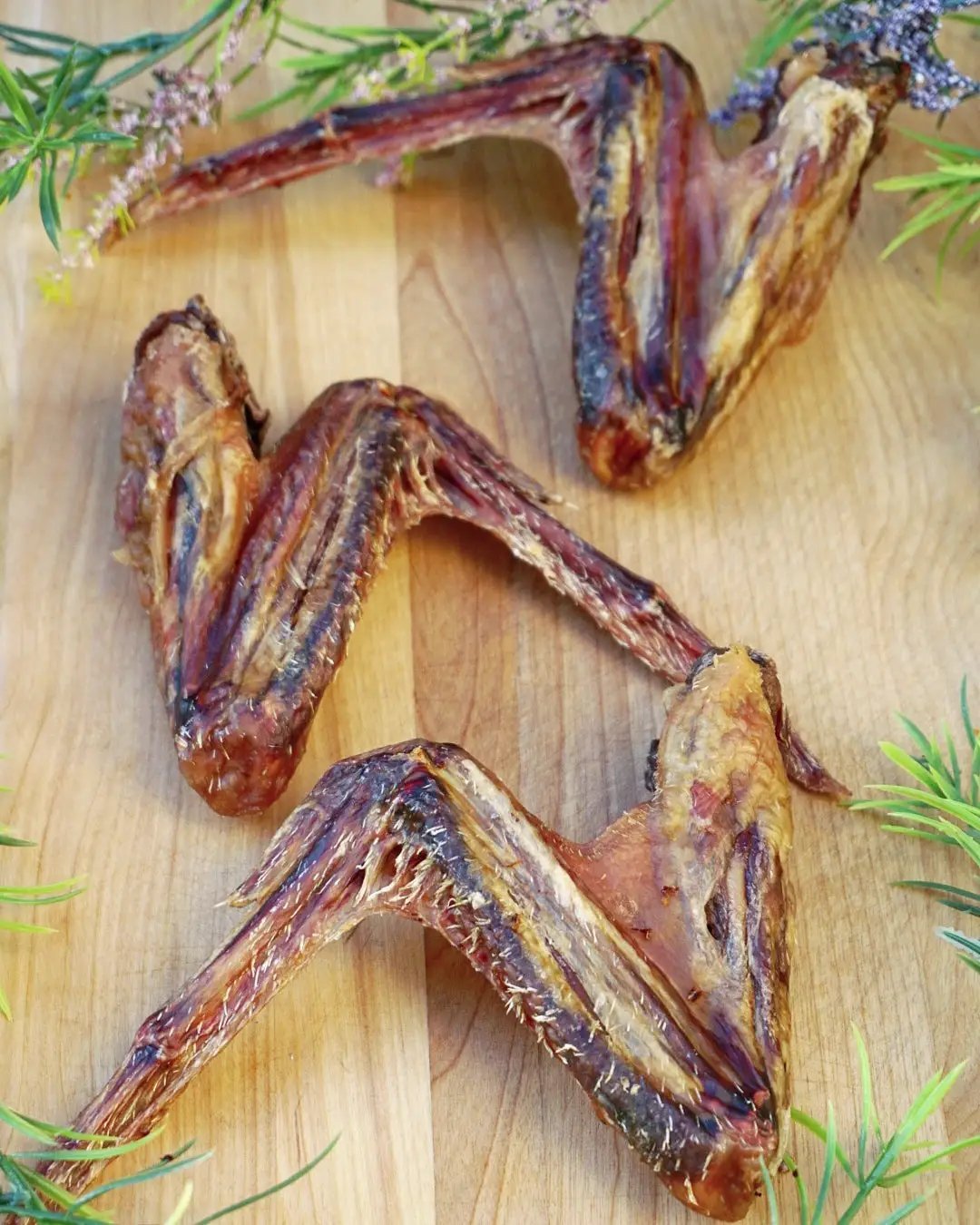 Duck Wings (ABF) four dried wings arranged on a wooden cutting board with rosemary sprigs