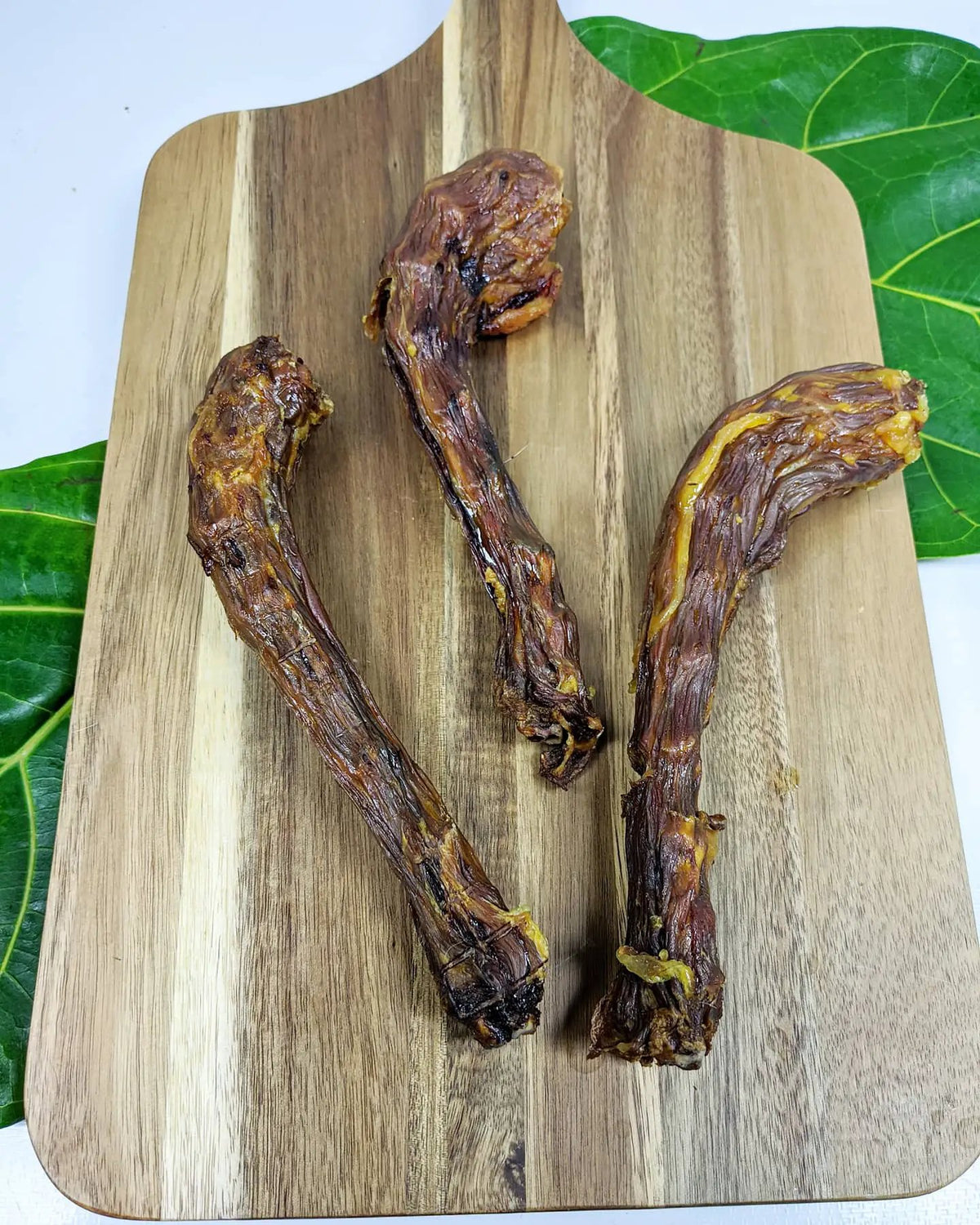Turkey neck jerky by Naked Beasts on a wooden cutting board, three dried neck pieces.