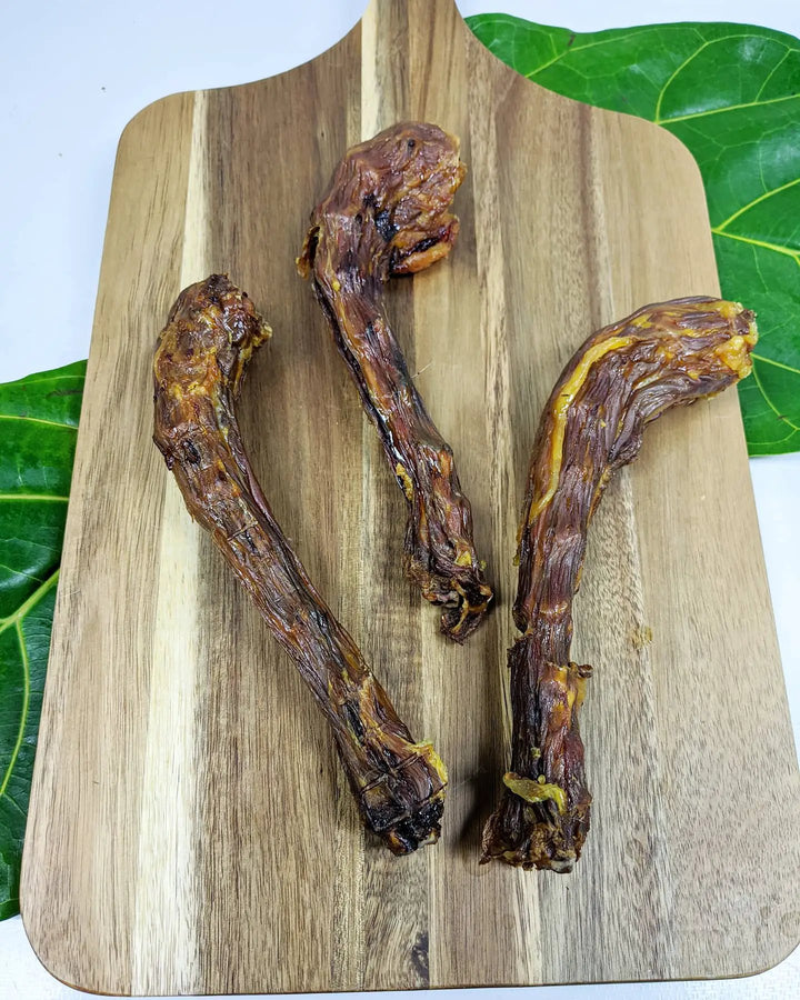 Turkey neck jerky by Naked Beasts on a wooden cutting board, three dried neck pieces.