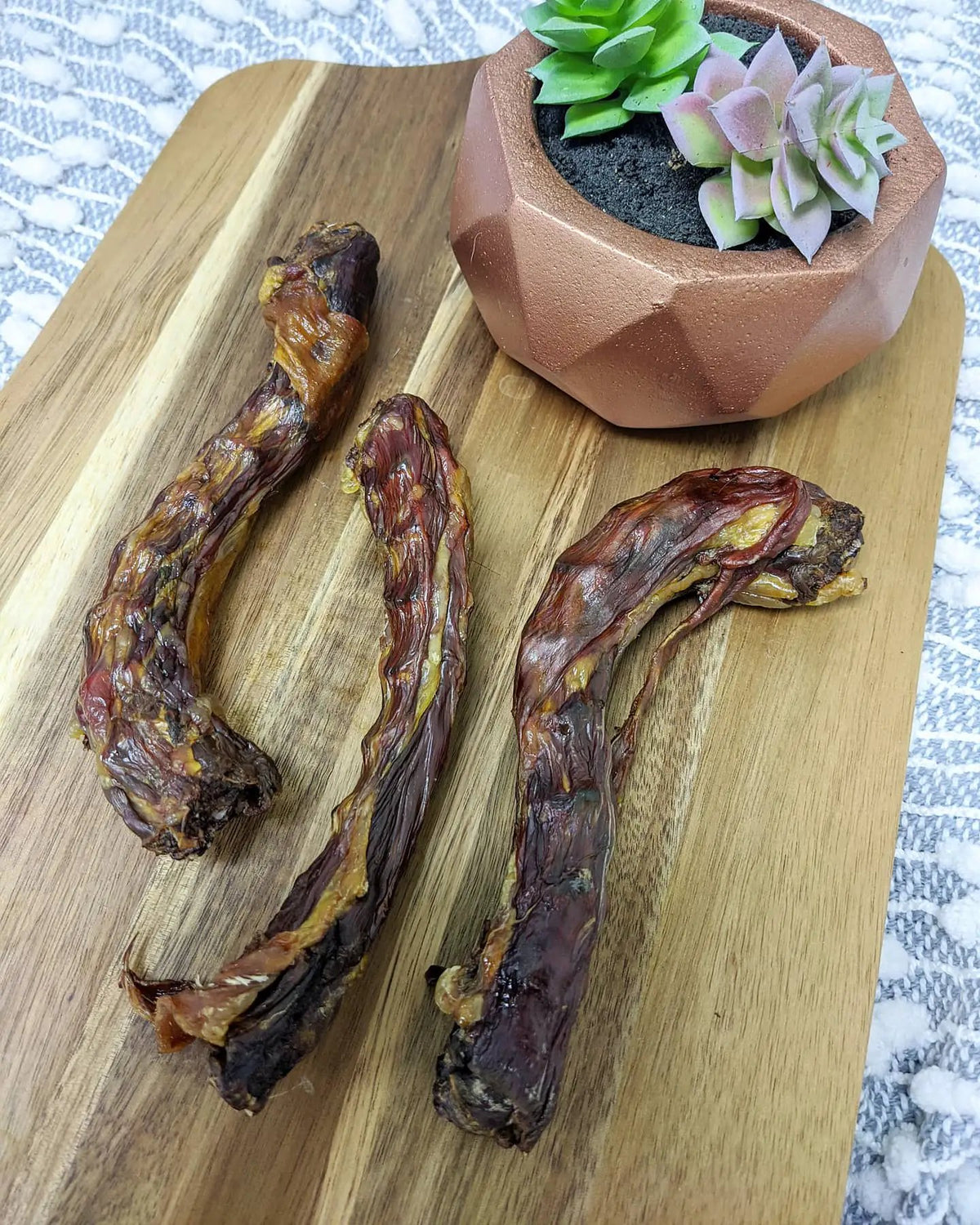 Duck Necks by Naked Beasts; four dried brown duck necks on a wooden board.