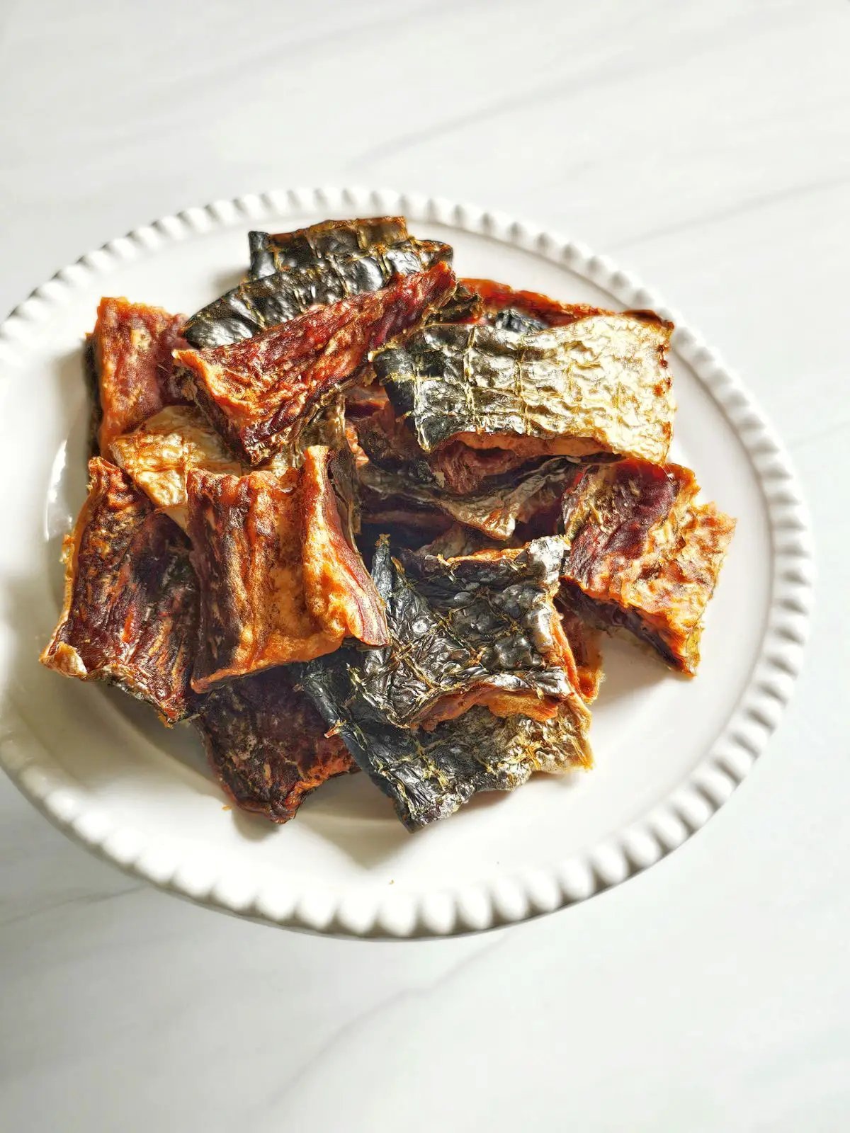 Salmon Fillet pieces by Naked Beasts, smoked and dried with crispy skin on a white plate