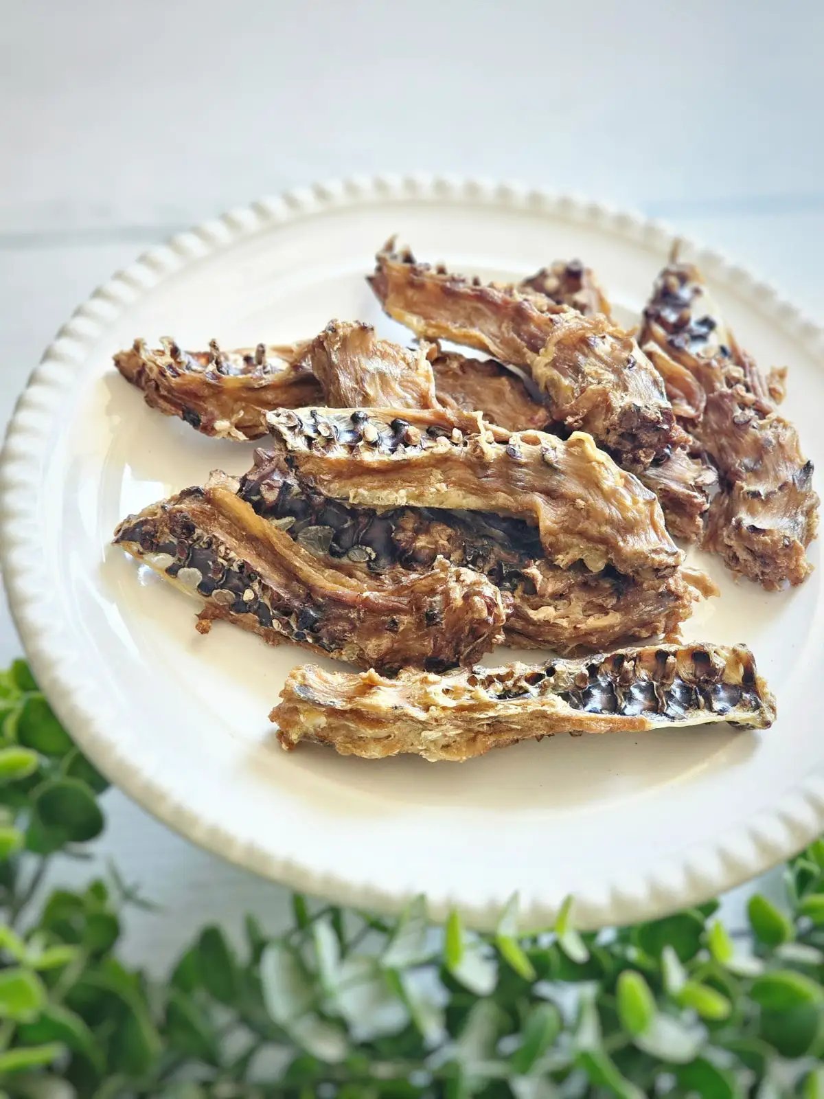 Naked Beasts Chicken Frames (Chunked) on a white plate with brown dried bone-in pieces