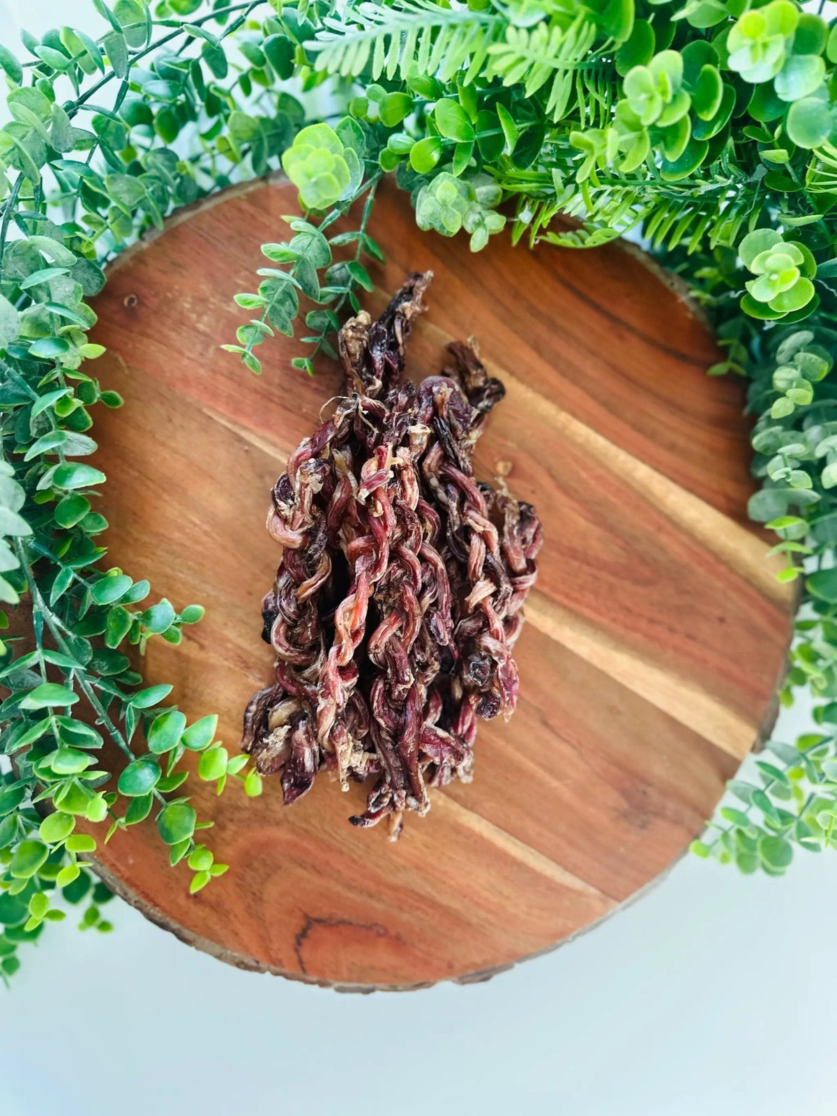Lamb Pizzle - Limited Edition, braided dried meat on a wooden board with lush greenery