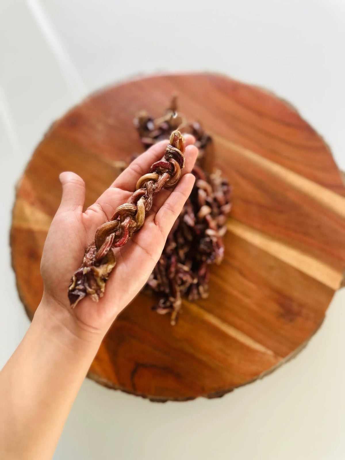 Lamb Pizzle - Limited Edition braided dried meat rope held in hand with a wooden board background