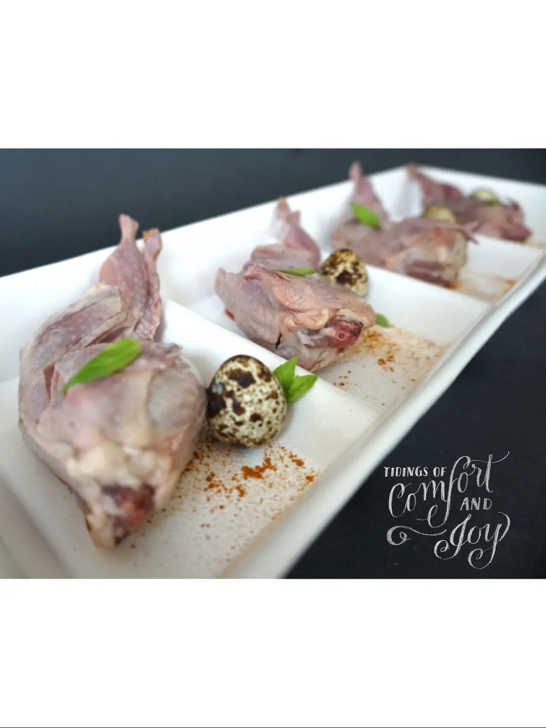 Whole quails (bone-in) by Naked Beasts on a white platter with quail eggs and herbs.