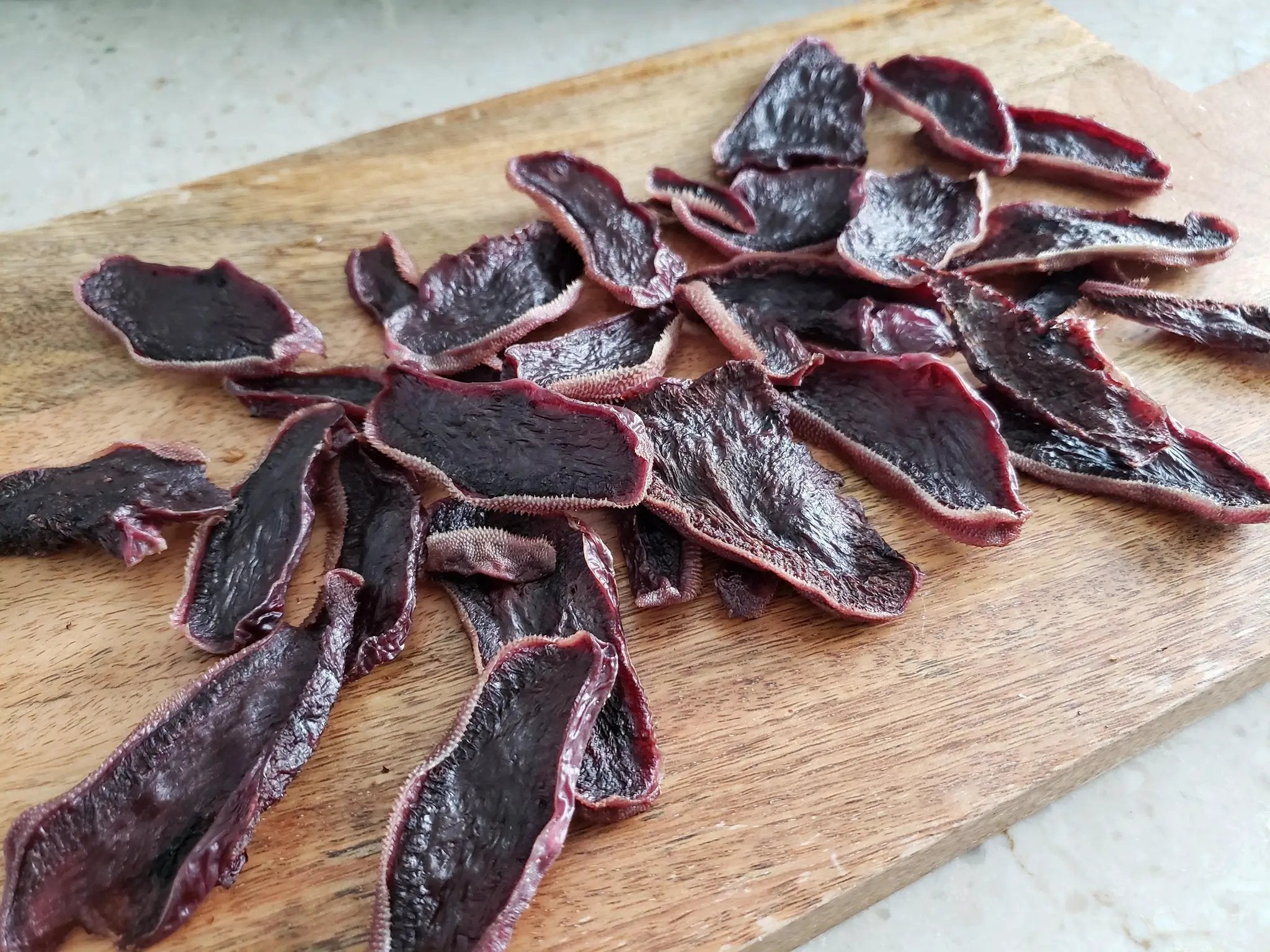 Beef tongue thin-cut slices by Naked Beasts on a wooden cutting board; dark red with pink edges