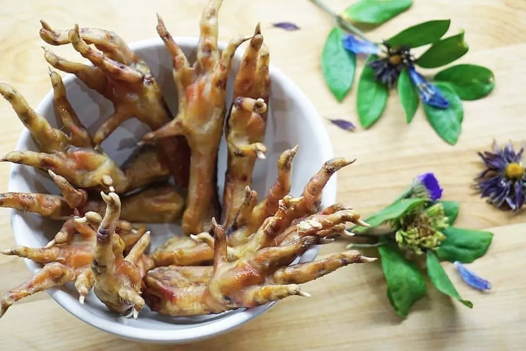 Chicken feet, Naked Beasts brand, golden-brown, several arranged in a white bowl.