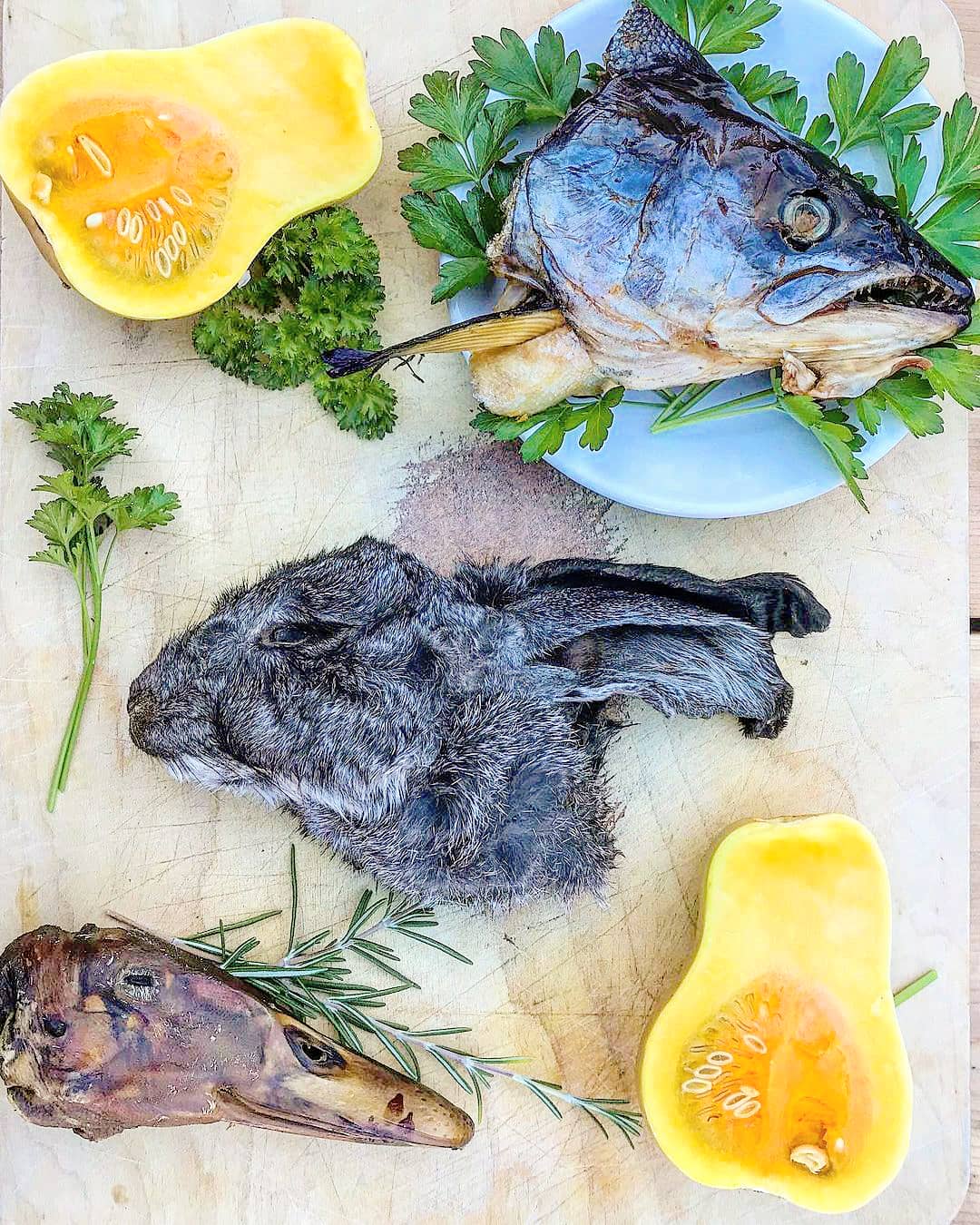 Salmon head halves on cutting board with parsley, rosemary, and yellow bell pepper halves.