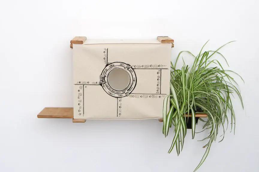 Deluxe Cat Cubby Bed, beige fabric with circular porthole opening mounted on wooden shelves.