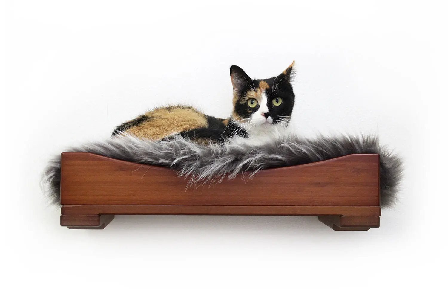 The Cat Nest Bed by Catastrophic Creations on a wooden cat shelf with plush gray faux-fur bed and a calico cat resting.