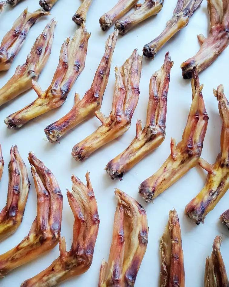 Dried duck feet laid out on a white background; brown-yellow, wrinkled feet with a leathery texture.