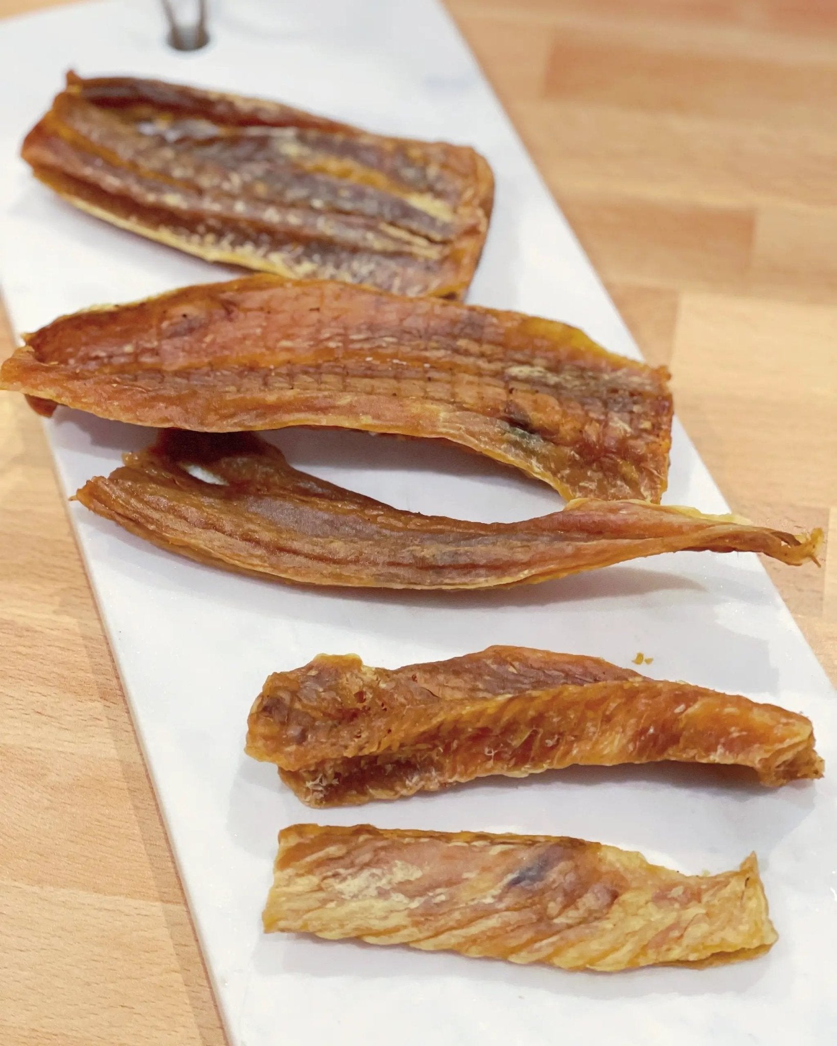 Naked Beasts hoki jerky, wild caught - 6 brown slices on a white plate