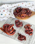 Load image into Gallery viewer, Limited Edition Beef Pizzle chews by Naked Beasts; sticks and loops in red dried form on a wooden board.
