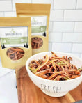 Load image into Gallery viewer, Carrot chips by Naked Beasts in a white bowl, orange dried slices with two Naked Beasts packages in the background.
