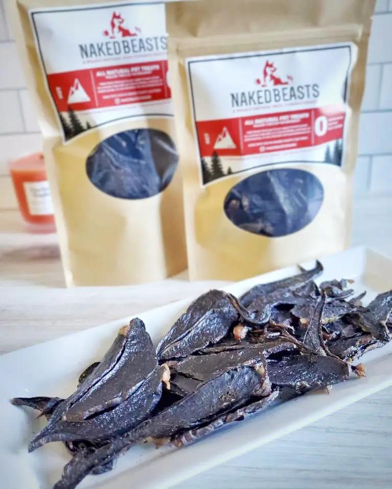 Lamb Spleen Thin Cut dog treats by Naked Beasts; dark dried strips on a plate with two Naked Beasts bags in the background.